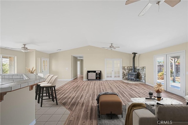 living area with ceiling fan, light wood-type flooring, lofted ceiling, french doors, and a wood stove