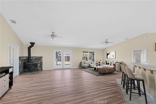 living area with a wood stove, a ceiling fan, visible vents, and french doors