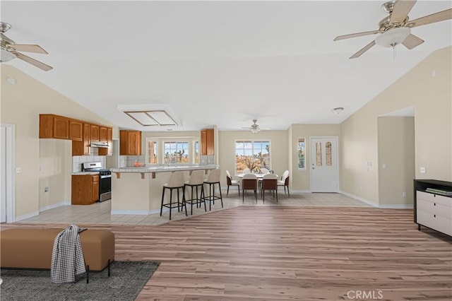 living area with baseboards, light wood-style floors, a ceiling fan, and vaulted ceiling