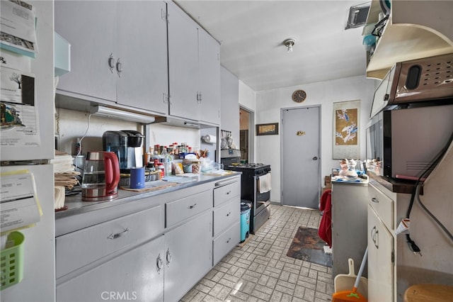 kitchen featuring stainless steel range with gas cooktop, freestanding refrigerator, light countertops, white cabinets, and brick patterned floor