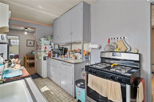 kitchen with brick patterned floor, a sink, freestanding refrigerator, gas stove, and white cabinets