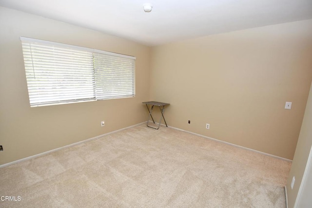 empty room featuring baseboards and light carpet