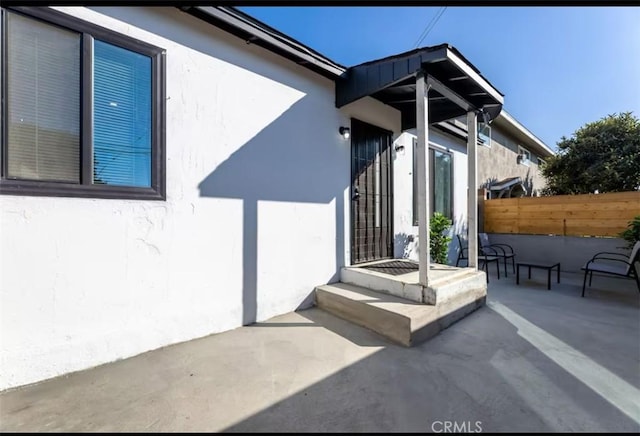 entrance to property featuring stucco siding, a patio, and fence