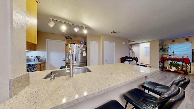 kitchen featuring visible vents, light stone counters, appliances with stainless steel finishes, a peninsula, and a sink