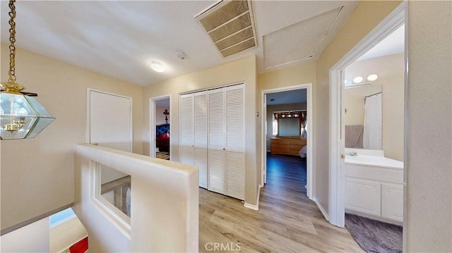 hall featuring visible vents, light wood-style flooring, baseboards, and a sink