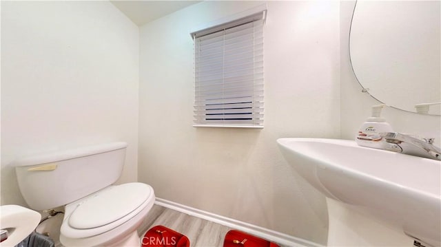 half bath featuring a sink, toilet, baseboards, and wood finished floors