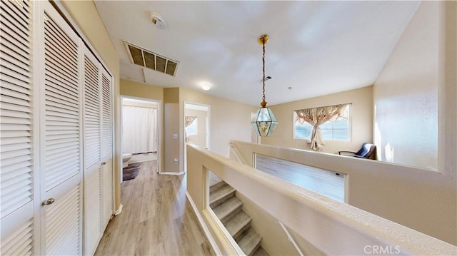 hall with visible vents, baseboards, attic access, an upstairs landing, and light wood-style floors