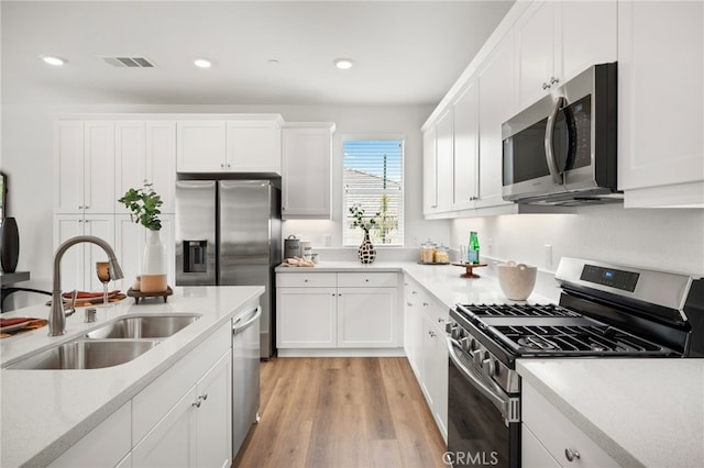 kitchen with light wood-style flooring, a sink, stainless steel appliances, light countertops, and white cabinetry