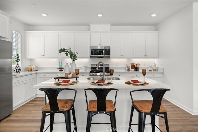 kitchen with a sink, wood finished floors, appliances with stainless steel finishes, a breakfast bar area, and light countertops