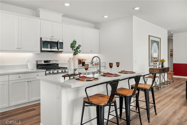 kitchen featuring a breakfast bar area, light wood-style floors, appliances with stainless steel finishes, and an island with sink