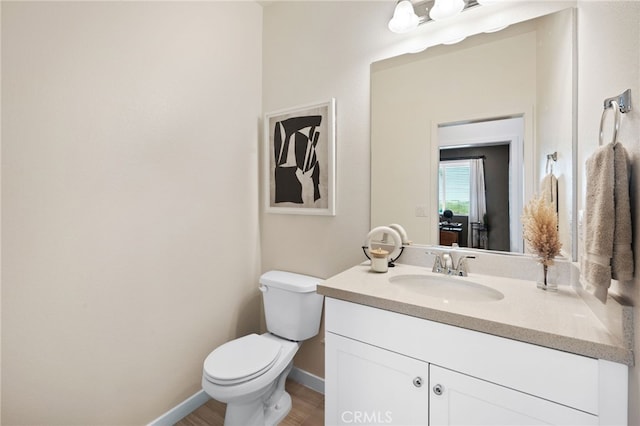 half bathroom featuring toilet, vanity, and baseboards