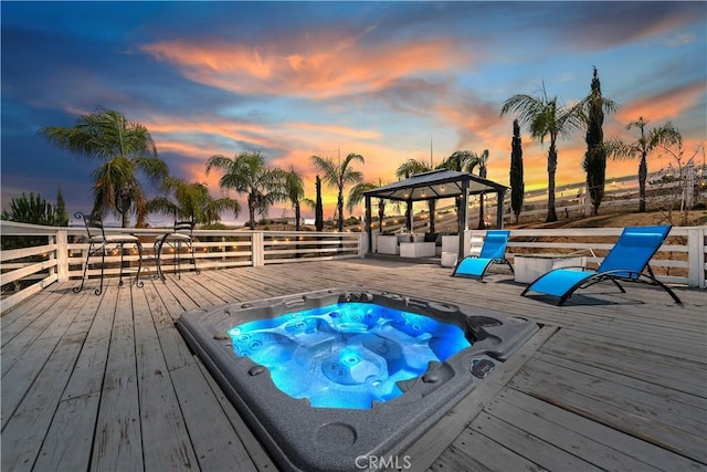 pool at dusk with a gazebo, a wooden deck, and hot tub deck surround