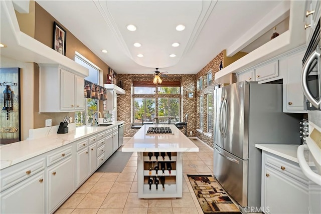 kitchen featuring brick wall, a kitchen island, light tile patterned flooring, recessed lighting, and a raised ceiling