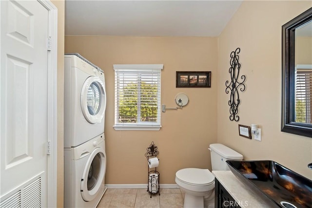 bathroom featuring tile patterned floors, visible vents, toilet, stacked washer / drying machine, and baseboards