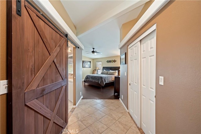 bedroom with light tile patterned floors, baseboards, lofted ceiling, ceiling fan, and a barn door