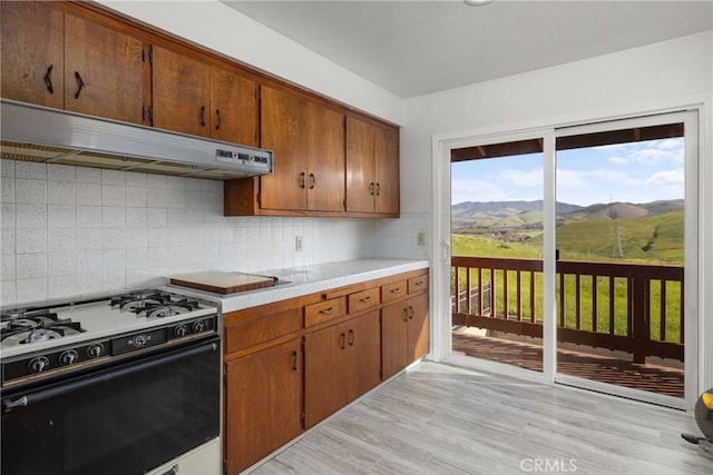 kitchen featuring decorative backsplash, light countertops, gas range oven, under cabinet range hood, and light wood-type flooring