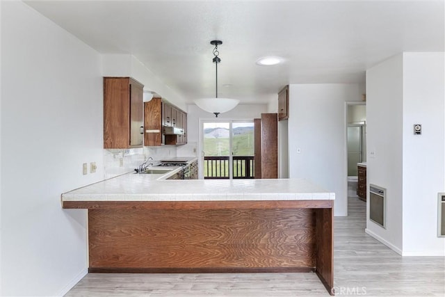 kitchen featuring brown cabinetry, a sink, extractor fan, light countertops, and backsplash