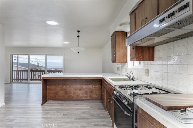 kitchen with under cabinet range hood, light countertops, a peninsula, gas stove, and a sink