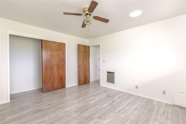 unfurnished bedroom with a closet, heating unit, baseboards, and light wood-style flooring