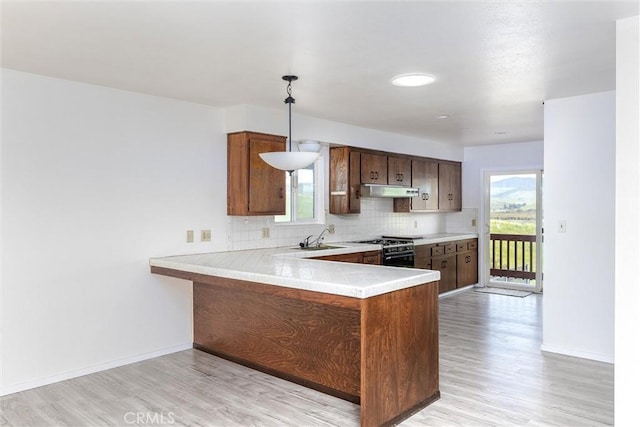 kitchen featuring under cabinet range hood, range with gas cooktop, a peninsula, light countertops, and decorative backsplash