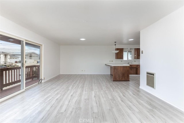 unfurnished living room with heating unit, plenty of natural light, baseboards, and light wood-style flooring