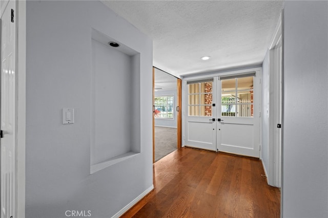 hallway featuring french doors, a textured ceiling, baseboards, and wood finished floors