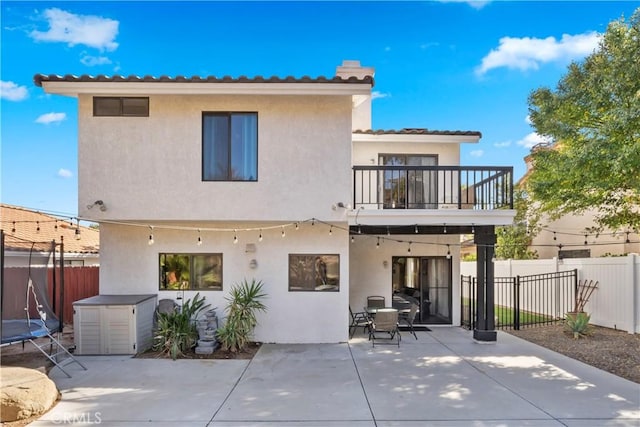 rear view of house featuring stucco siding, a trampoline, a balcony, and a patio area