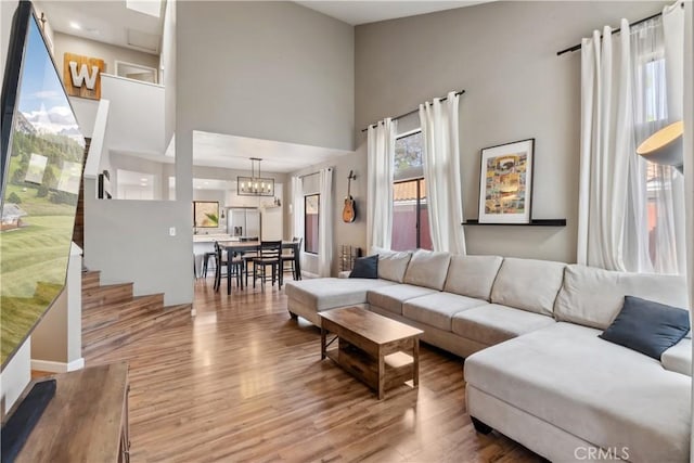 living area featuring stairway, wood finished floors, a high ceiling, and a chandelier