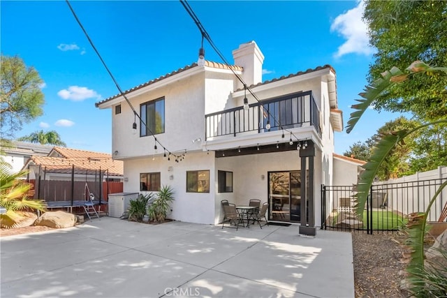 back of property with a patio, a balcony, fence, stucco siding, and a trampoline