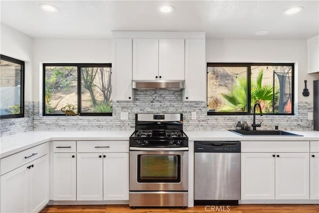 kitchen with under cabinet range hood, light countertops, appliances with stainless steel finishes, white cabinetry, and a sink