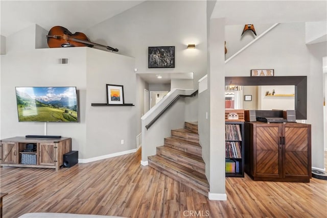 staircase featuring visible vents, high vaulted ceiling, baseboards, and wood finished floors