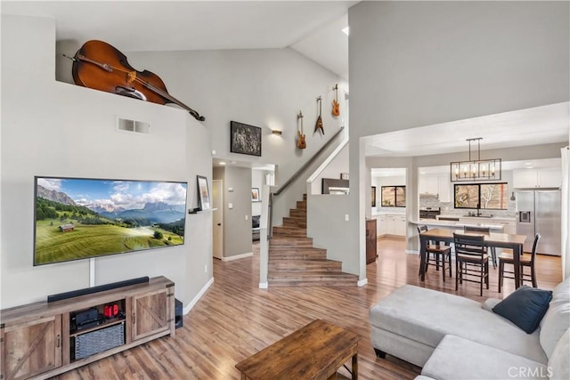 living room featuring visible vents, light wood-style floors, high vaulted ceiling, and stairway