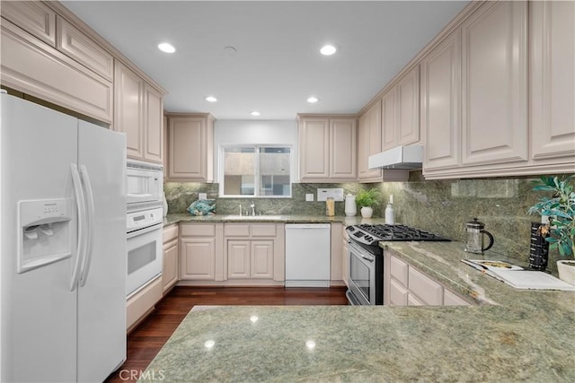 kitchen featuring white appliances, light stone countertops, dark wood-style floors, a sink, and under cabinet range hood