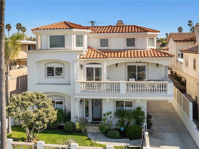 mediterranean / spanish-style home featuring a tile roof, a balcony, fence, and stucco siding