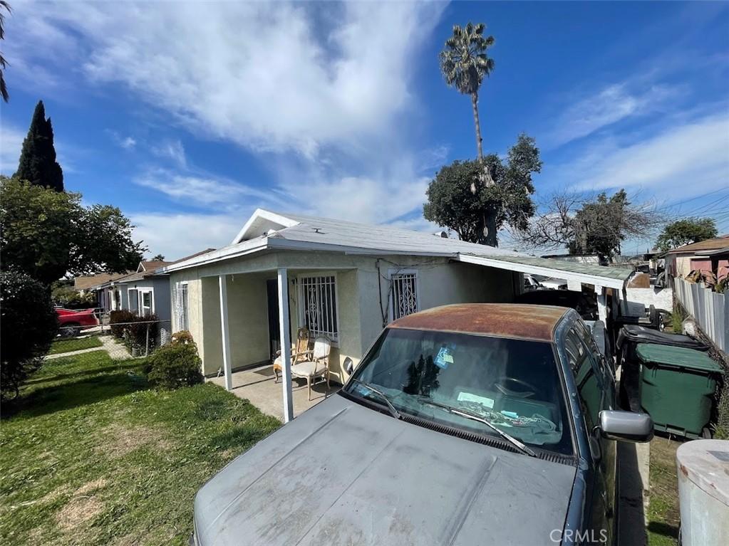 view of front of property featuring stucco siding, an attached carport, a front lawn, and fence