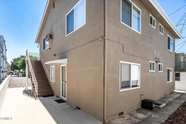 view of side of home featuring stucco siding, stairs, and fence