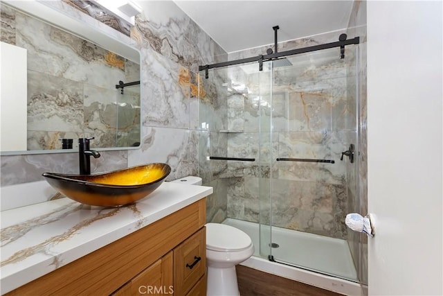 bathroom featuring a marble finish shower, tasteful backsplash, toilet, vanity, and tile walls