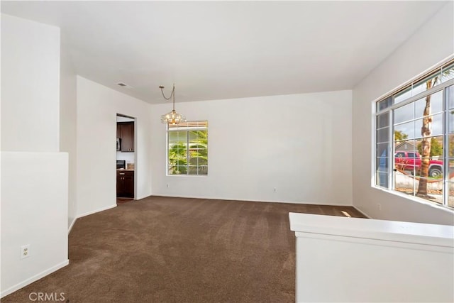 empty room featuring dark colored carpet, visible vents, baseboards, and an inviting chandelier