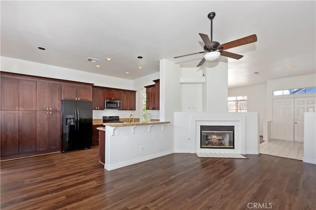 kitchen with a breakfast bar, stainless steel microwave, a peninsula, stove, and black refrigerator with ice dispenser