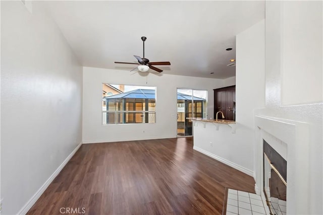 unfurnished living room featuring a ceiling fan, a tiled fireplace, wood finished floors, and baseboards