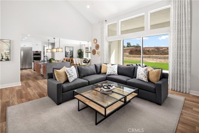 living room featuring recessed lighting, baseboards, high vaulted ceiling, and light wood finished floors