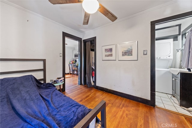 bedroom with a sink, ceiling fan, ornamental molding, stacked washer / dryer, and light wood-type flooring