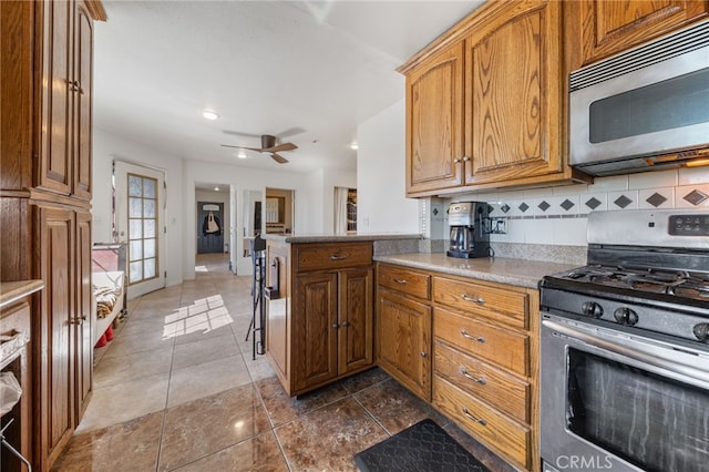 kitchen with ceiling fan, decorative backsplash, brown cabinets, stainless steel appliances, and dark tile patterned flooring