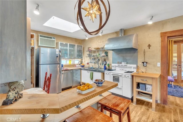 kitchen featuring an AC wall unit, appliances with stainless steel finishes, a skylight, light wood-style floors, and wall chimney exhaust hood