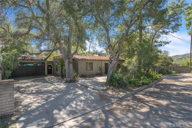 mediterranean / spanish-style home featuring a tile roof, fence, and stucco siding