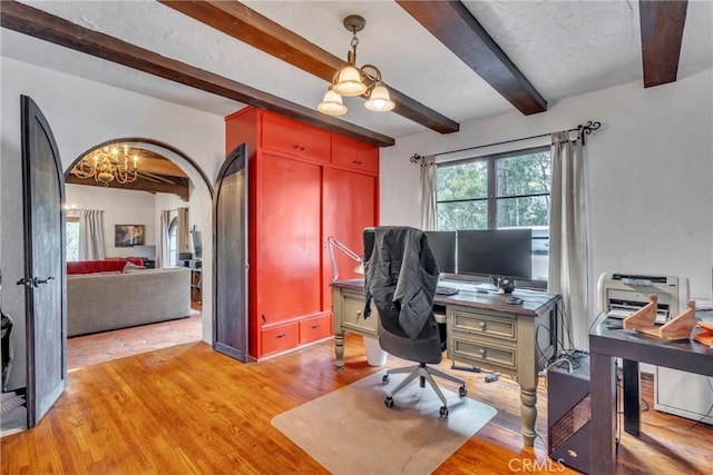 office area featuring beamed ceiling, light wood-style floors, an inviting chandelier, arched walkways, and a textured ceiling