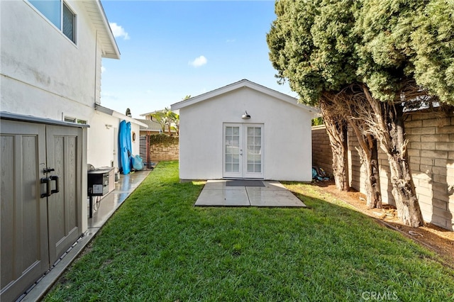 back of house featuring stucco siding, an outbuilding, a lawn, a fenced backyard, and french doors