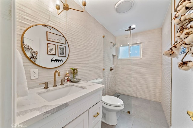 bathroom with toilet, a tile shower, tile walls, tile patterned flooring, and vanity