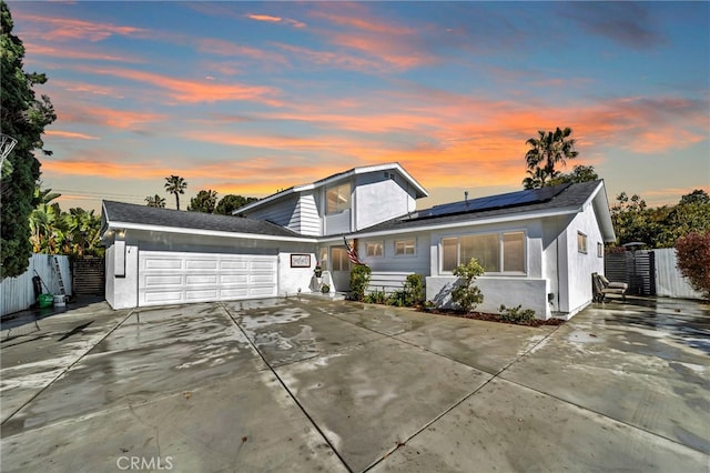 traditional-style home featuring solar panels, concrete driveway, an attached garage, and fence