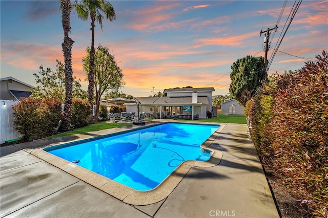 pool at dusk featuring a patio, fence, an outdoor pool, and an outdoor structure